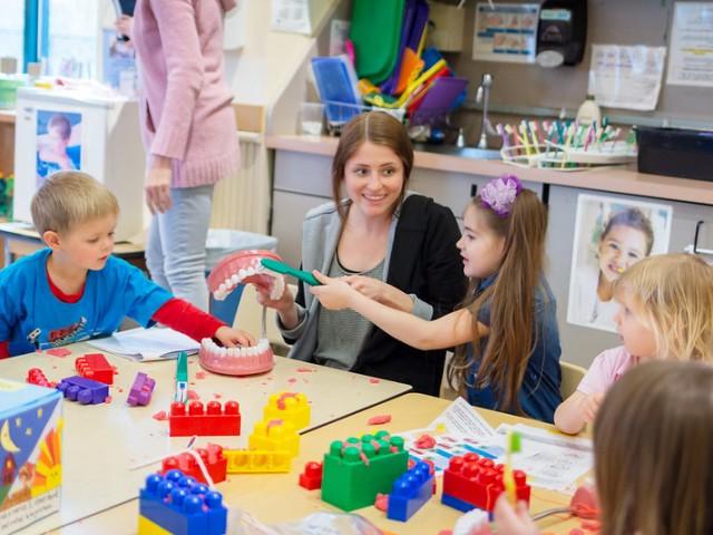 teaching assistant sitting at table with children while playing with building blocks